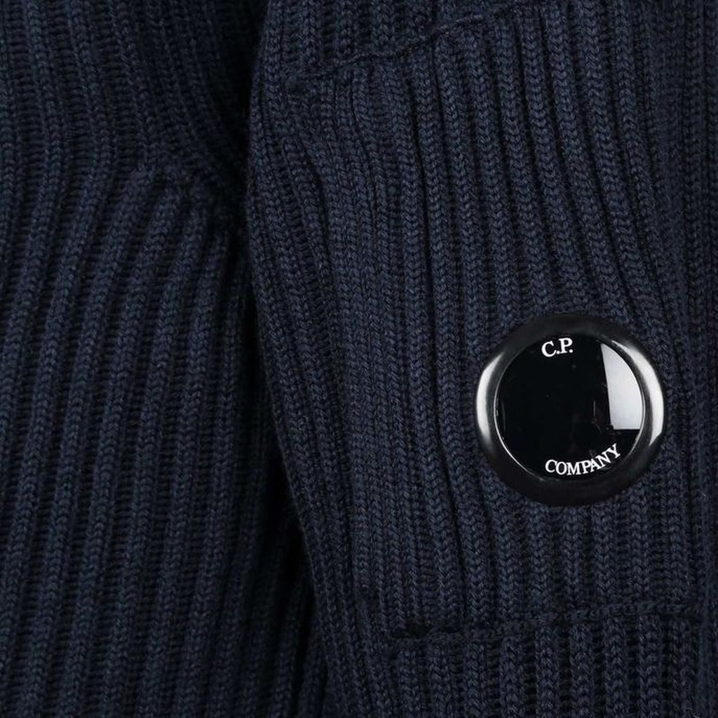 Close-up of the iconic CP Company goggle on the zipped side pocket of the blue wool turtleneck sweater.
