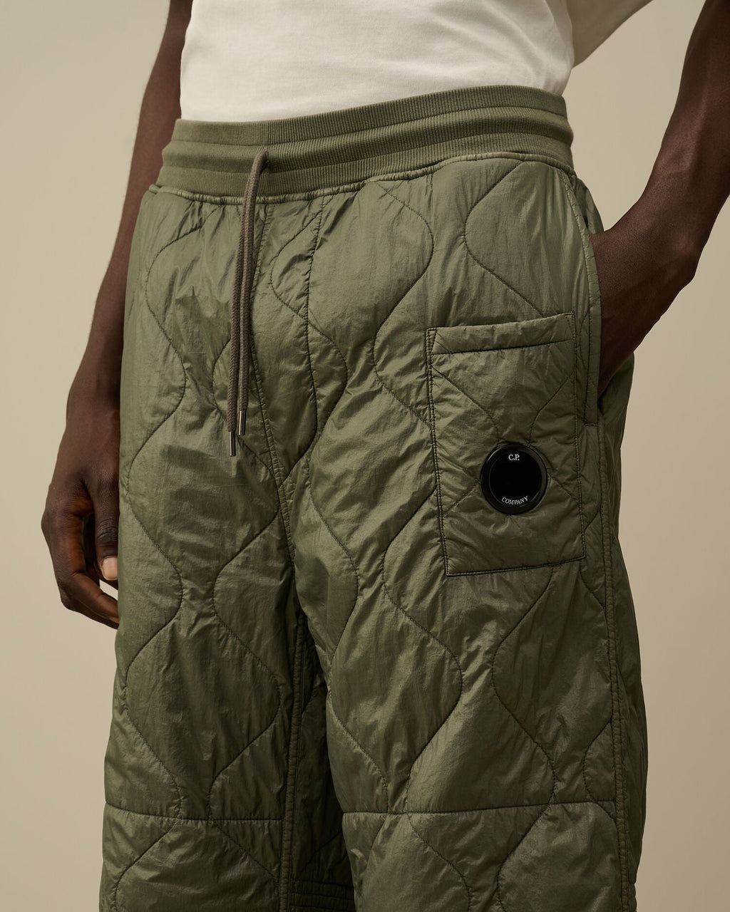Close-up of the iconic CP Company lens detail on the pocket of the camo green quilted sweatpants.

