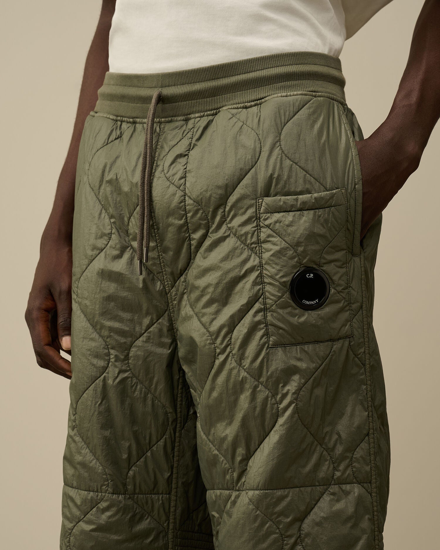 Close-up of the iconic CP Company lens detail on the pocket of the camo green quilted sweatpants.
