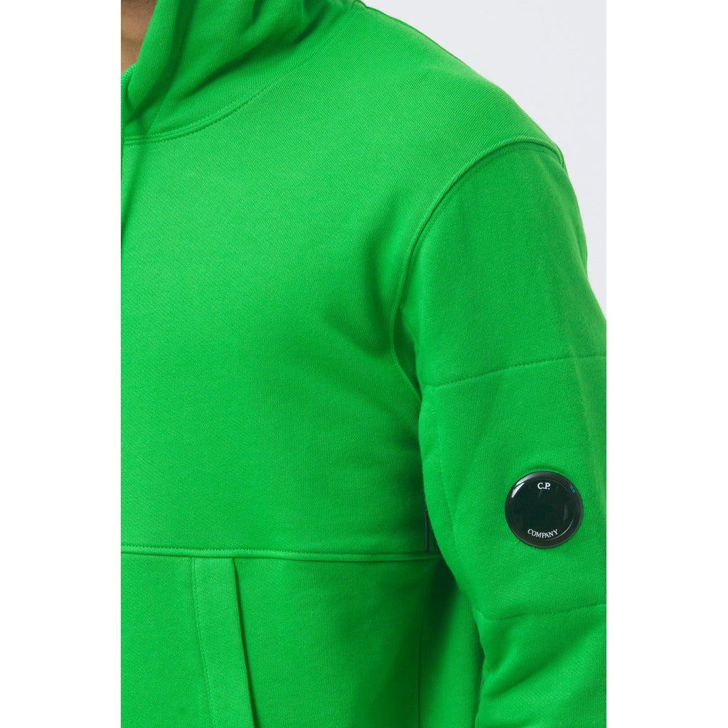 Close-up of the iconic CP Company goggle on the side zipped pocket of the green cotton hoodie.
