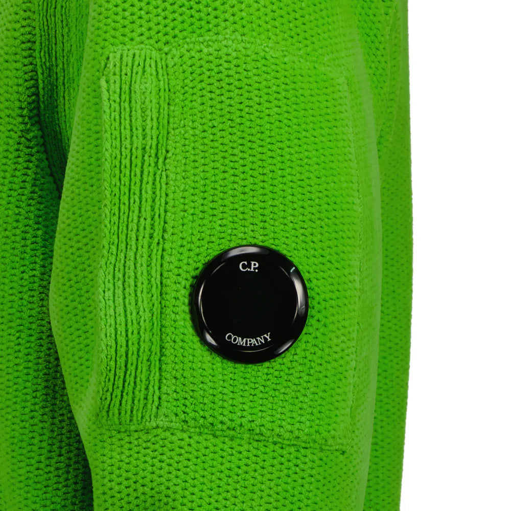 Close-up of the iconic CP Company goggle on the side zip pocket of the green wool blend sweater.
