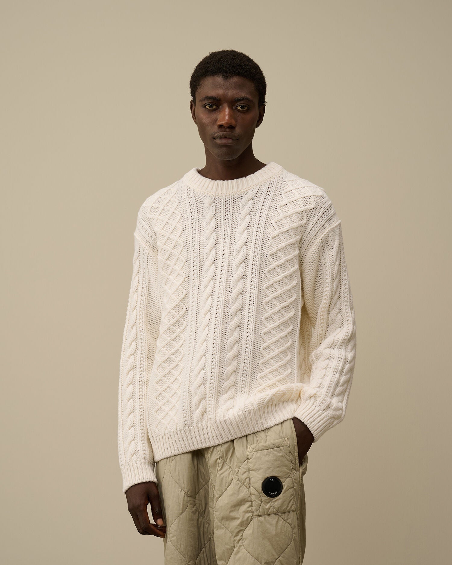 Model showcasing the regular fit of the CP Company cream white cable-knit logo sweater.
