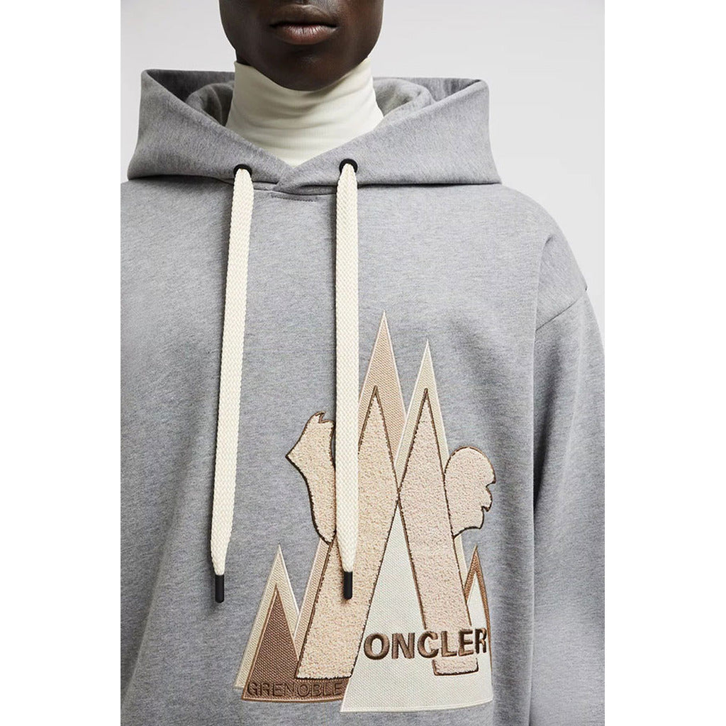 Close-up of the Moncler Grenoble logo patch on the gray hoodie