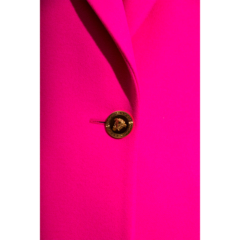 Close-up detail of the Versace logo buttons on the fuchsia coat.
